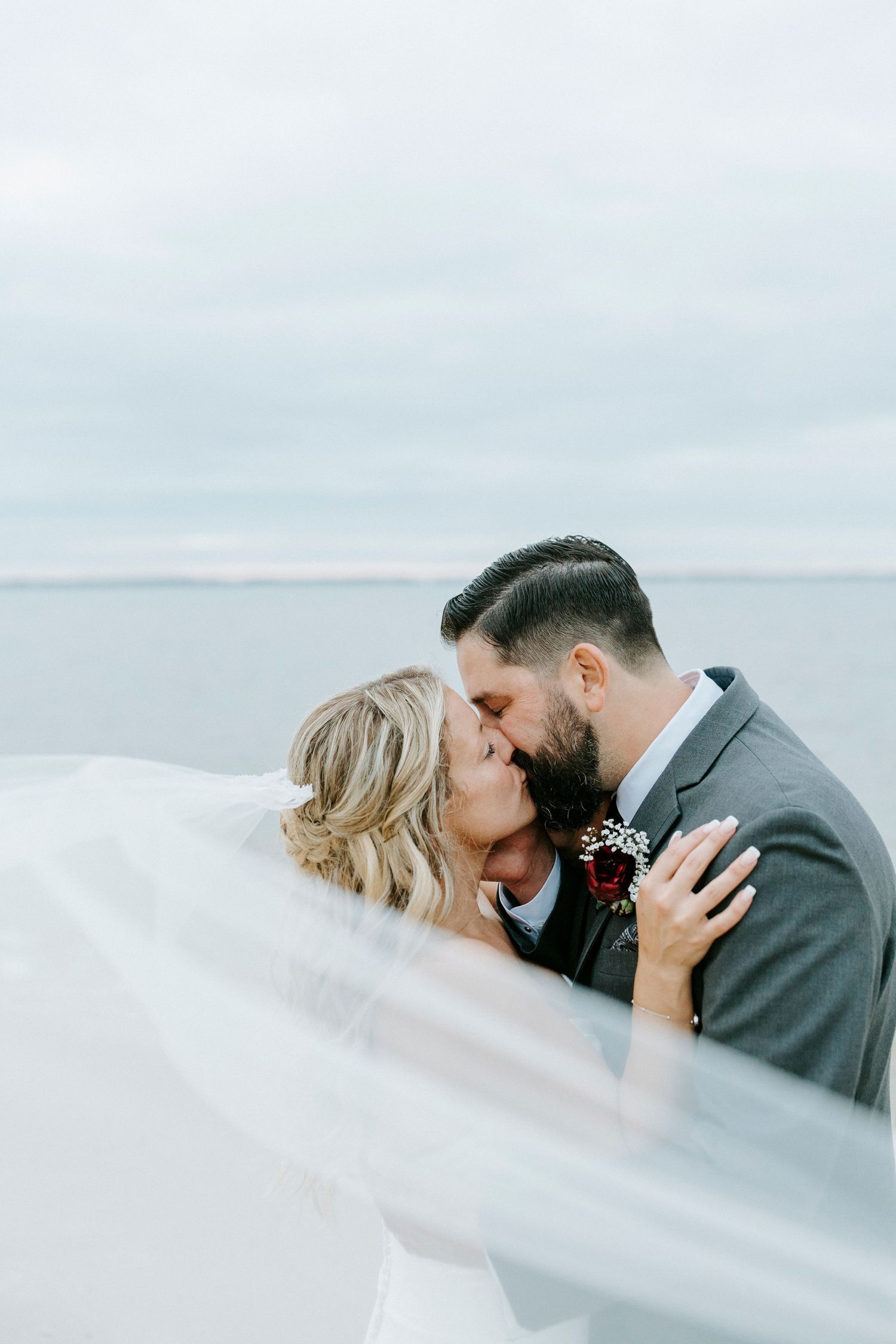 Ethereal wedding photo with flowing veil against misty coastal backdrop.