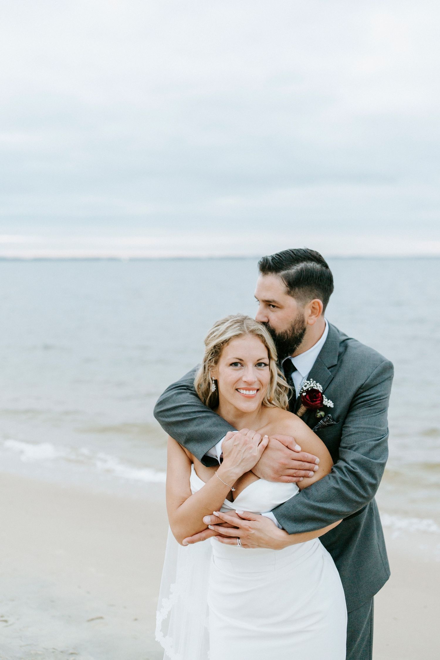 Joyful beachside wedding embrace with waves and cloudy sky in background.