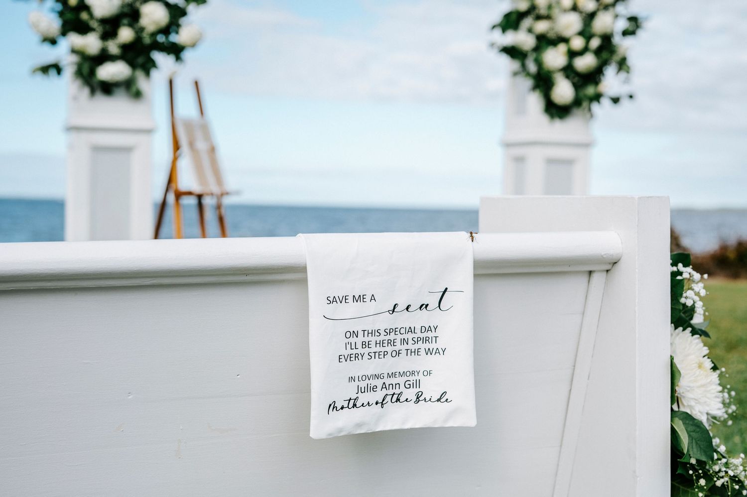 Wedding ceremony setup with white pergola and floral arrangements against a cloudy sky.