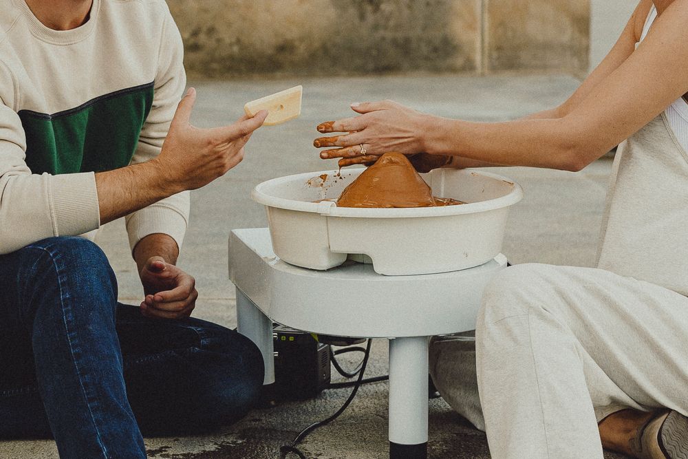Hands of people working with clay on pottery wheels in a bright ceramic studio class.