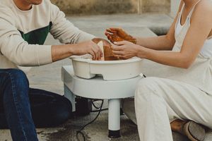 A couple sits together on a rooftop working with clay pottery on a white table.