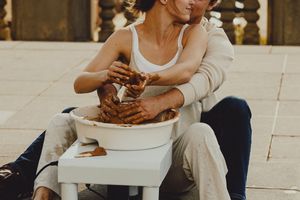 Hands work with clay on a pottery wheel against an urban backdrop.