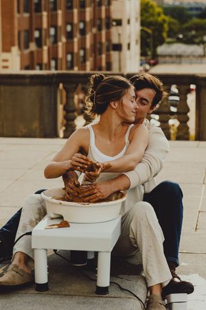 A couple enjoys pottery making together on a sunny rooftop with city buildings in view.