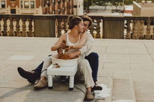 Couple works together on pottery wheel during sunset rooftop date in urban setting.