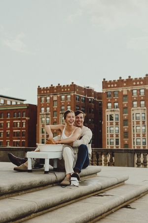 A couple shares a playful moment on a rooftop terrace with classic brick buildings in the background.