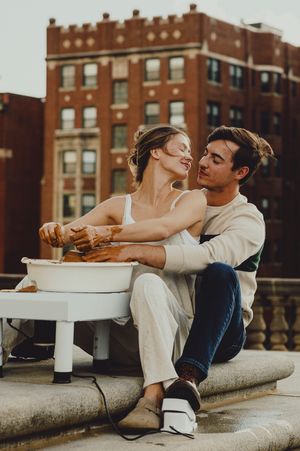 A couple relaxes on concrete steps with a small white table, surrounded by historic brick architecture.