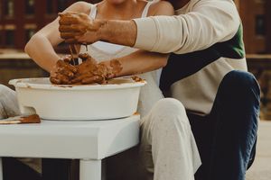 Close-up of hands working clay on white pottery wheel against urban backdrop.