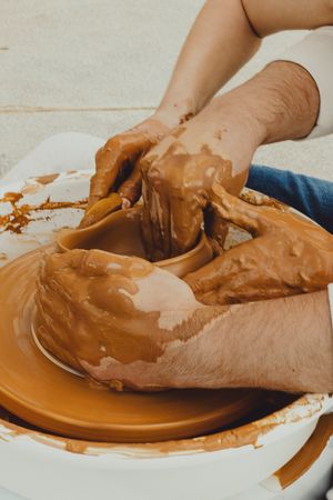 Close-up of hands working with brown clay on a ceramic pottery wheel.
