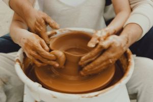 Close-up of hands working together to shape clay on a pottery wheel outdoors.