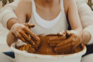 Hands shape clay on a pottery wheel during an outdoor session.