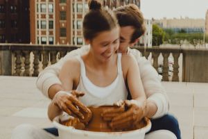Couple shares joyful moment while working with clay on rooftop pottery wheel.
