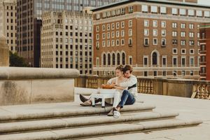 Couple works on pottery project against cityscape backdrop on stone steps.