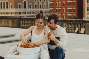 Intimate rooftop dining scene with couple enjoying food on a concrete ledge overlooking city architecture.