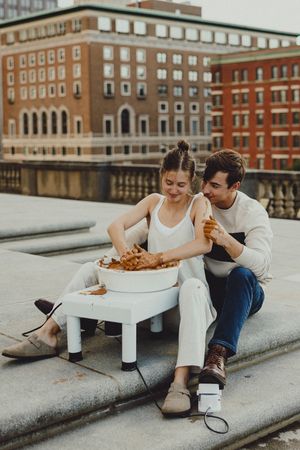 Couple enjoys pottery making session on urban rooftop with brick buildings in background.