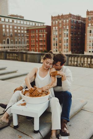 A couple shares a pottery making experience on a rooftop with urban architecture behind them.