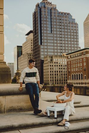 Urban rooftop date featuring couple dining at small table with downtown skyline and modern buildings in background.