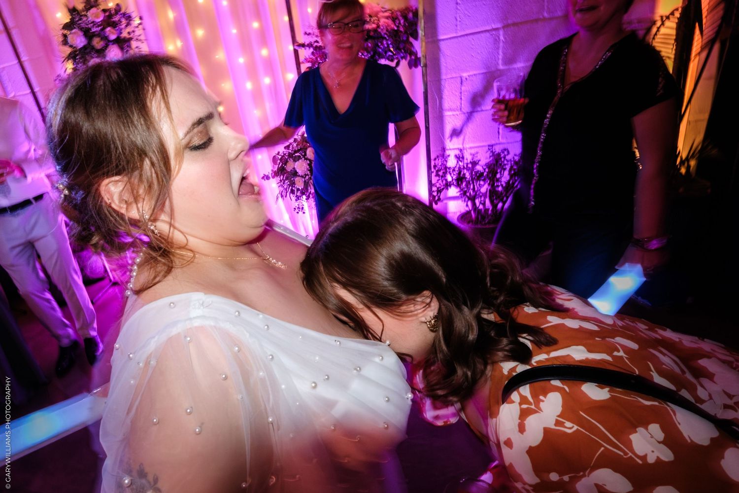 A group of people dancing and celebrating at a wedding reception with vibrant purple lighting and festive atmosphere.