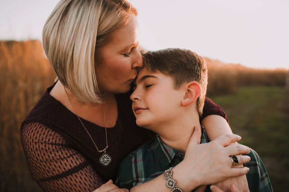 Tender moment of mother kissing son during golden hour portrait.