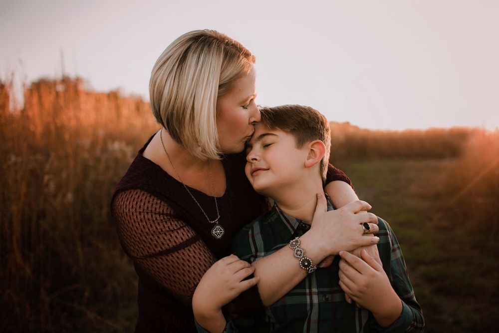 Mother hugging son in field during golden hour.