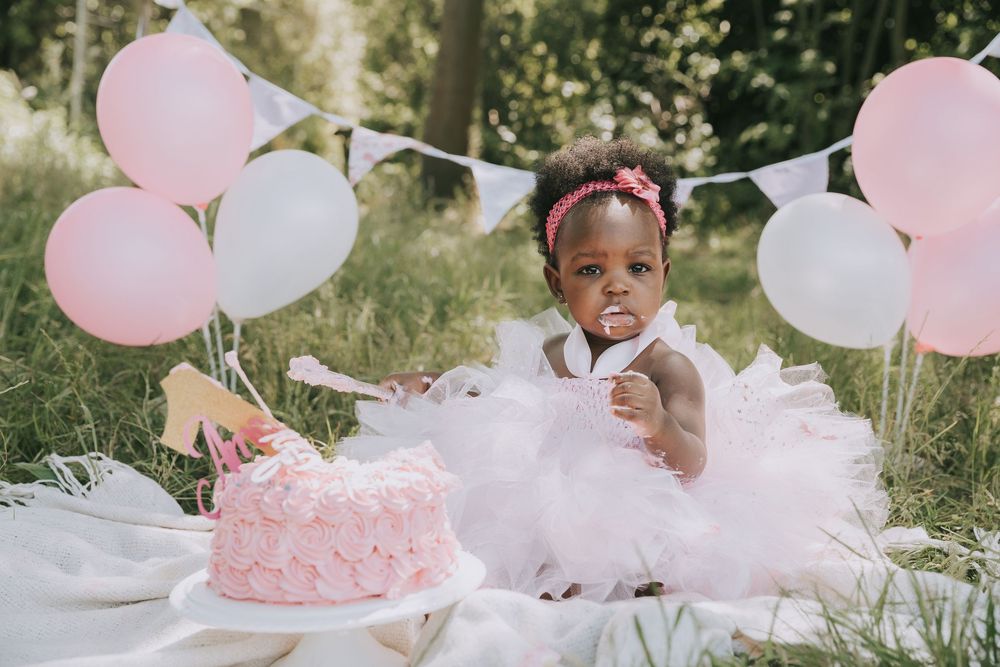 A pink and white themed first birthday celebration with balloons, tulle decorations and a smash cake in an outdoor setting.