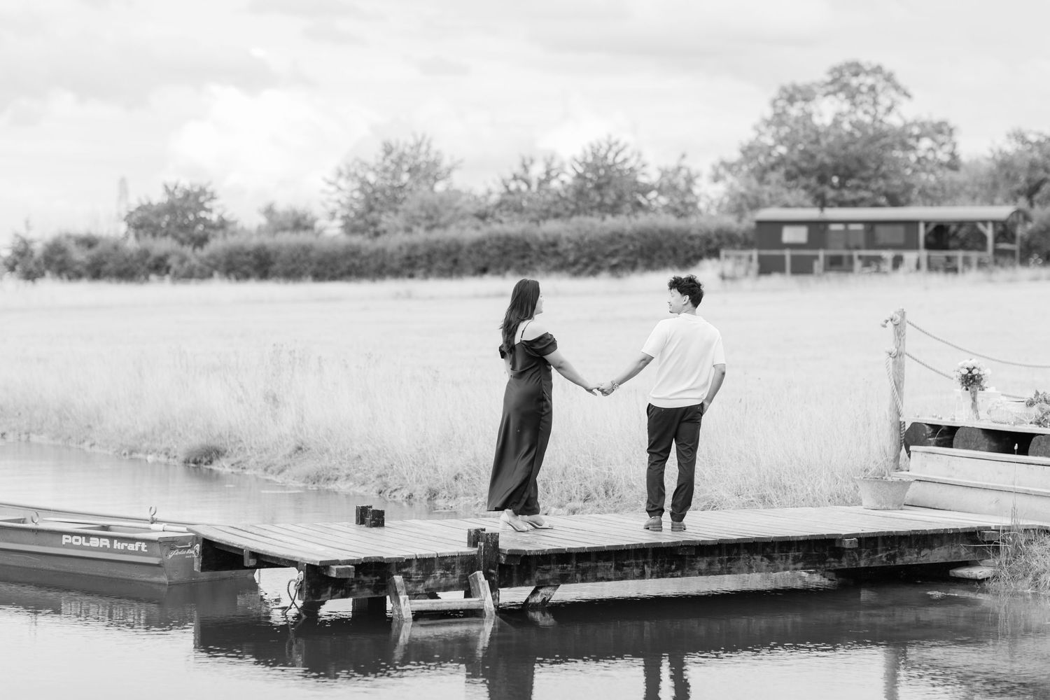 Newly engaged couple walking on a dock by a lake with boat in the background. Private estate Cotswolds Proposal. Hayley Elizabeth Photograph
