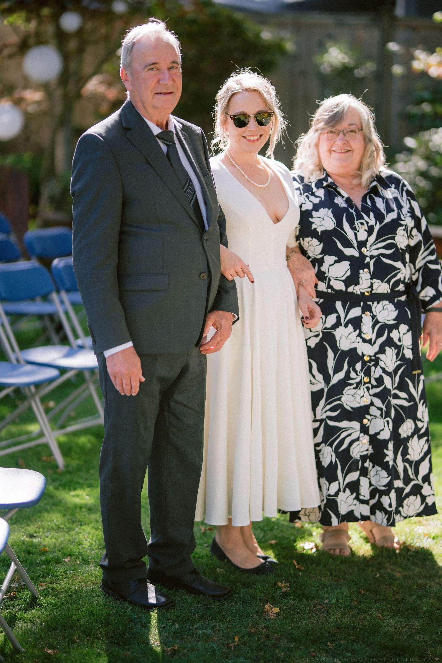 Wedding party members in formal attire posing together on grass during an outdoor garden ceremony.