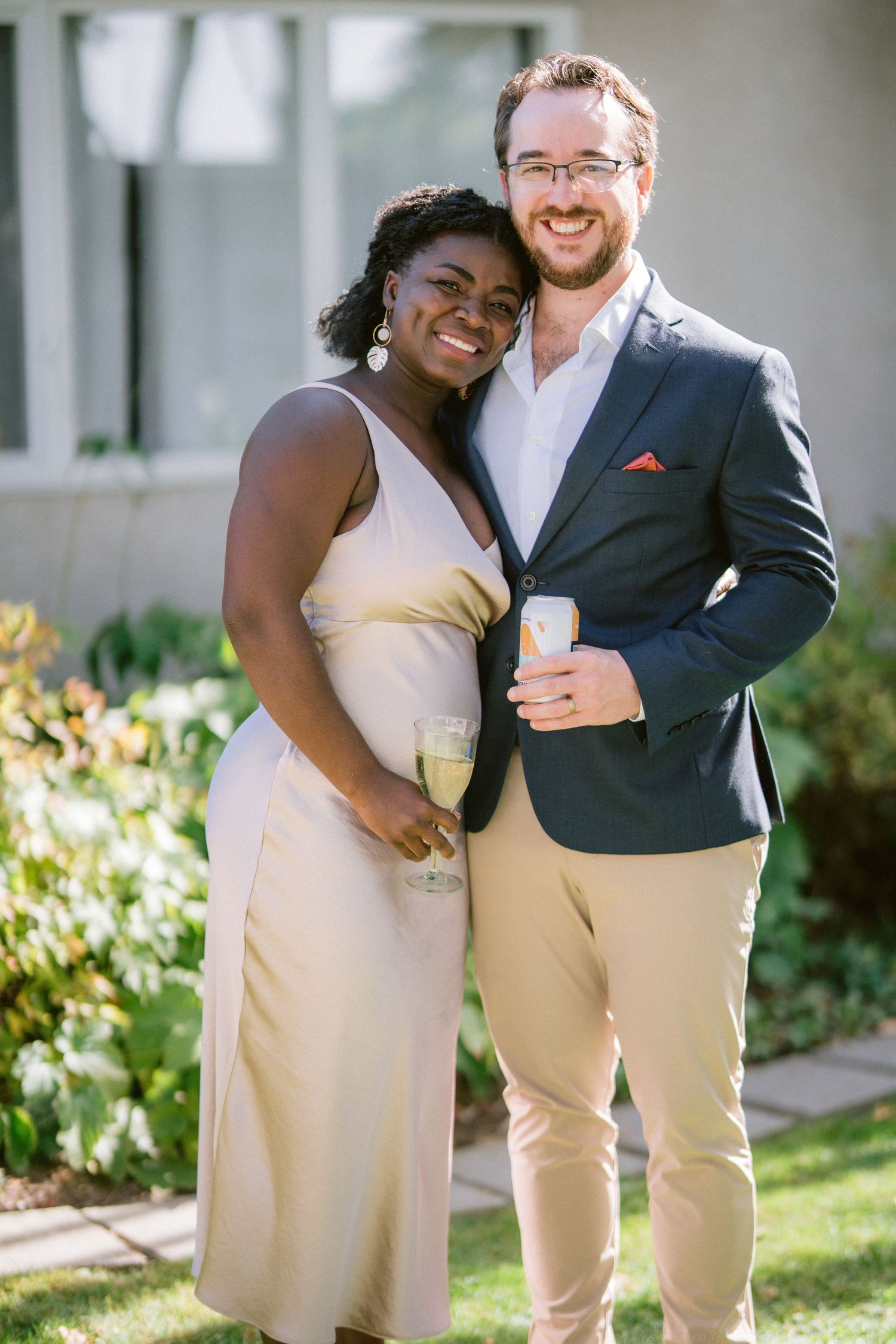 Happy couple in formal attire embracing on sunny garden pathway.