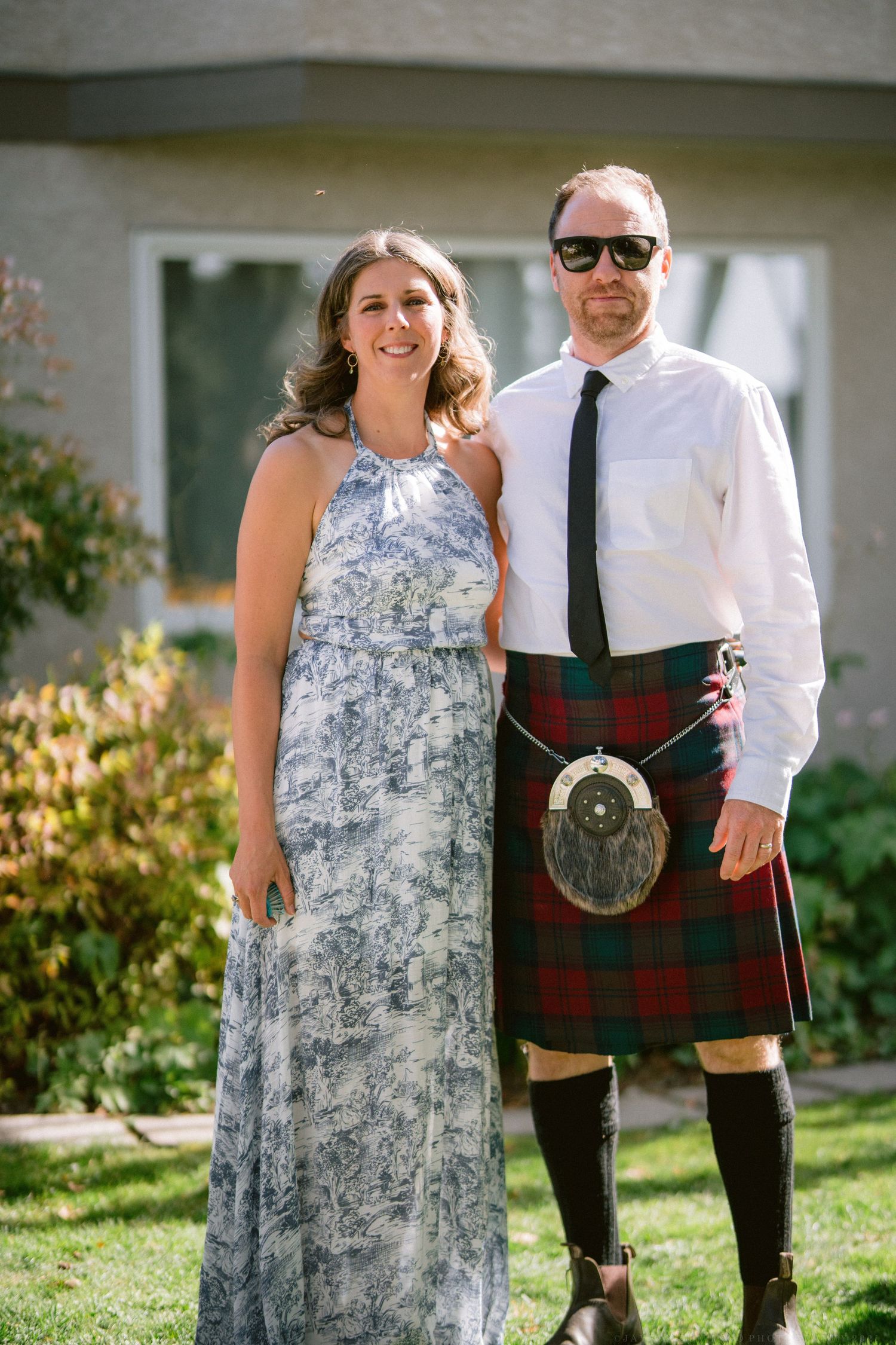 A couple poses outdoors, with one wearing a traditional Scottish kilt and sporran.