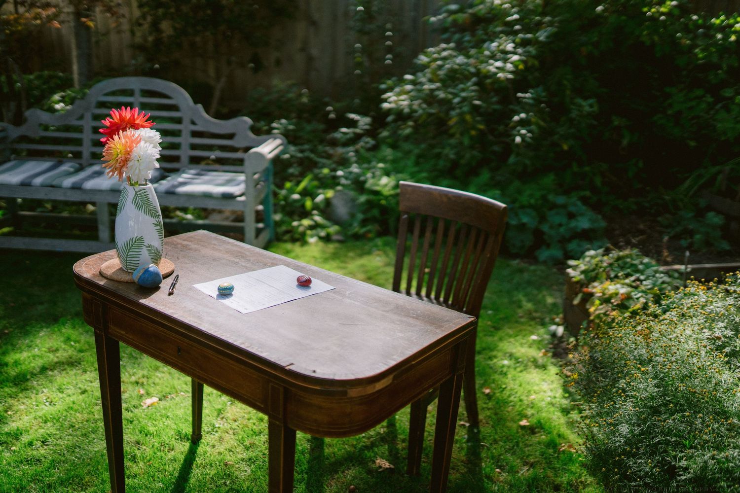 Wooden tables and chairs set up in shaded outdoor garden setting.