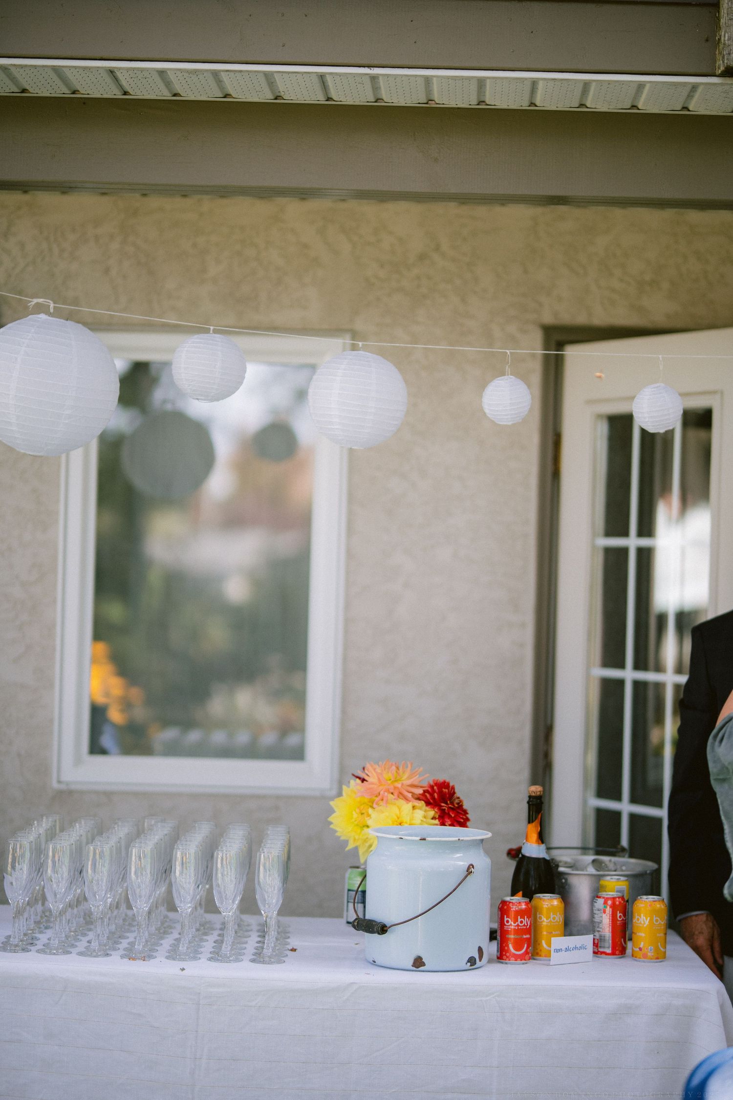 White paper lanterns and empty glasses line up on outdoor reception table.