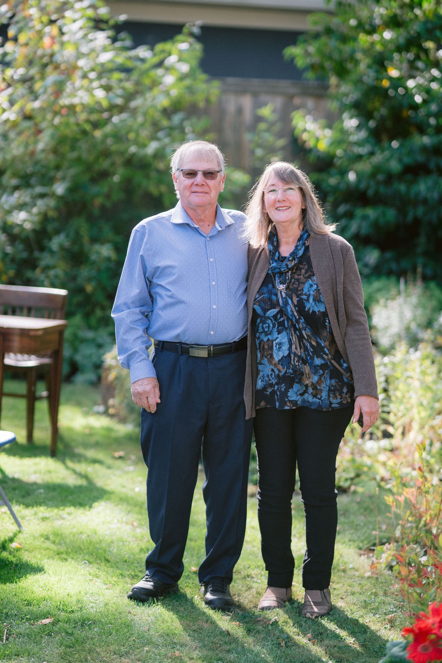 Couple sitting together outdoors on a sunny day with green foliage in the background.