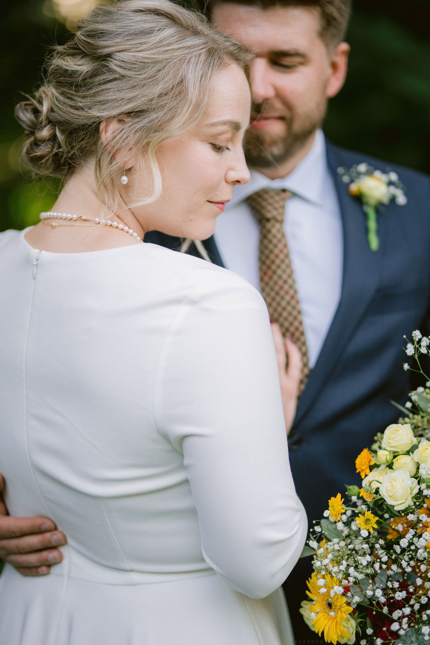 Couple embraces during an intimate outdoor wedding ceremony with yellow and white floral bouquet details.