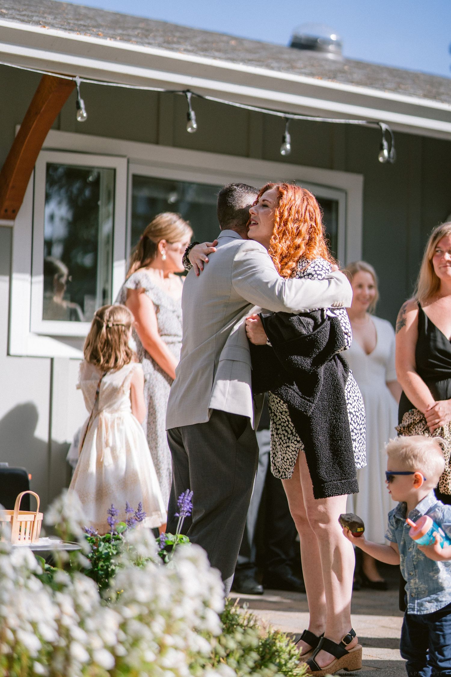 Wedding guests embrace and celebrate during an outdoor reception gathering.