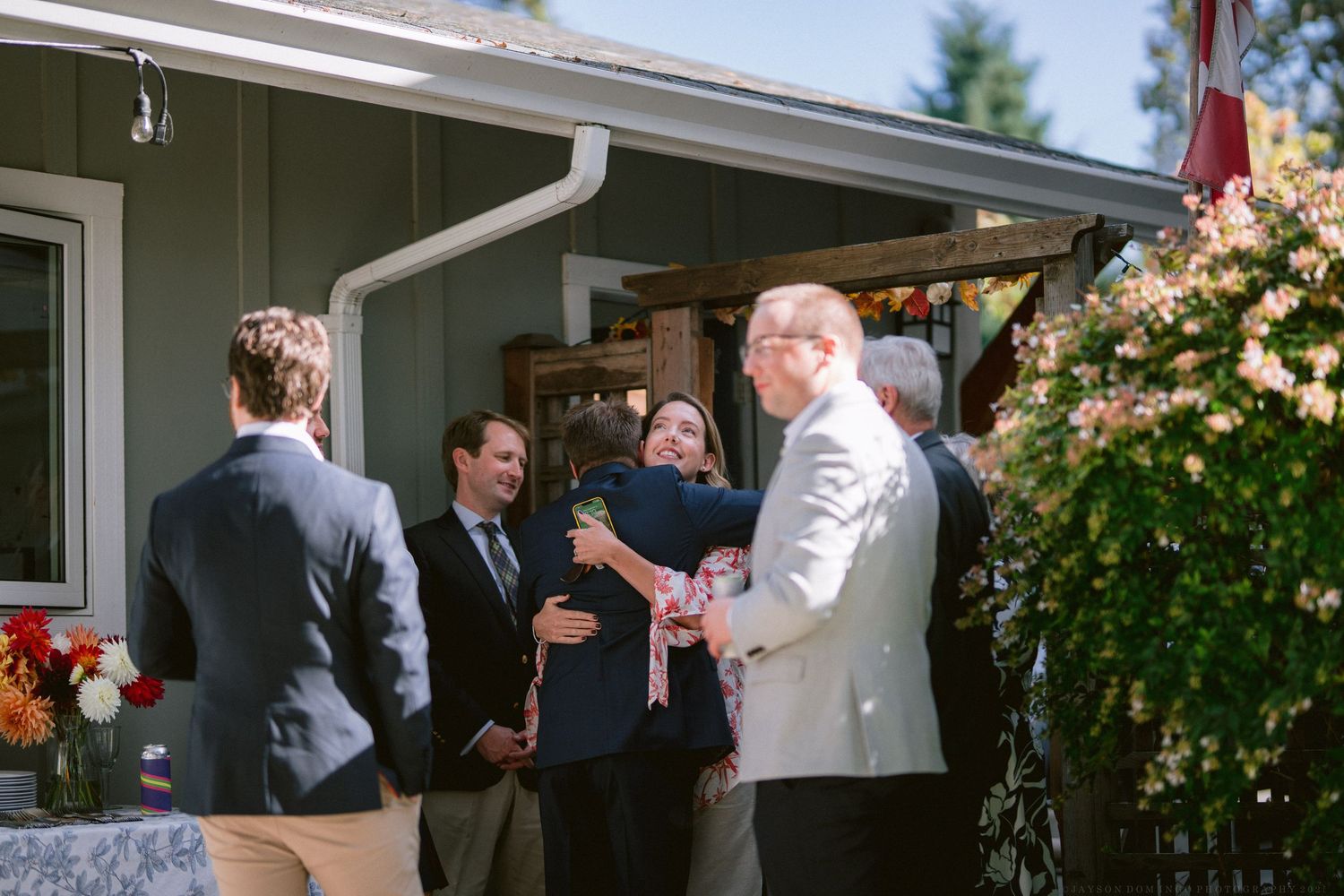 Wedding guests mingling on a porch with climbing roses and greenery in the background.