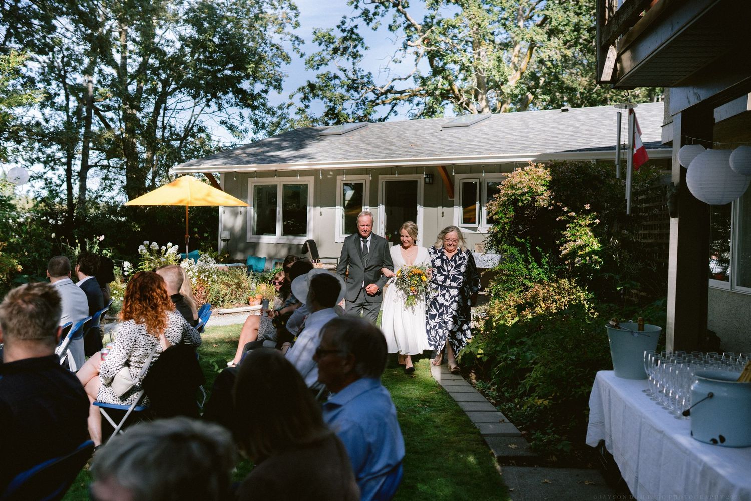 Outdoor event setup with white tents and tables arranged on a lawn near a building.