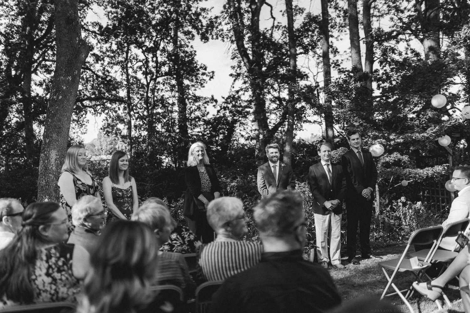 Outdoor wedding ceremony taking place in a wooded setting with rows of white chairs.