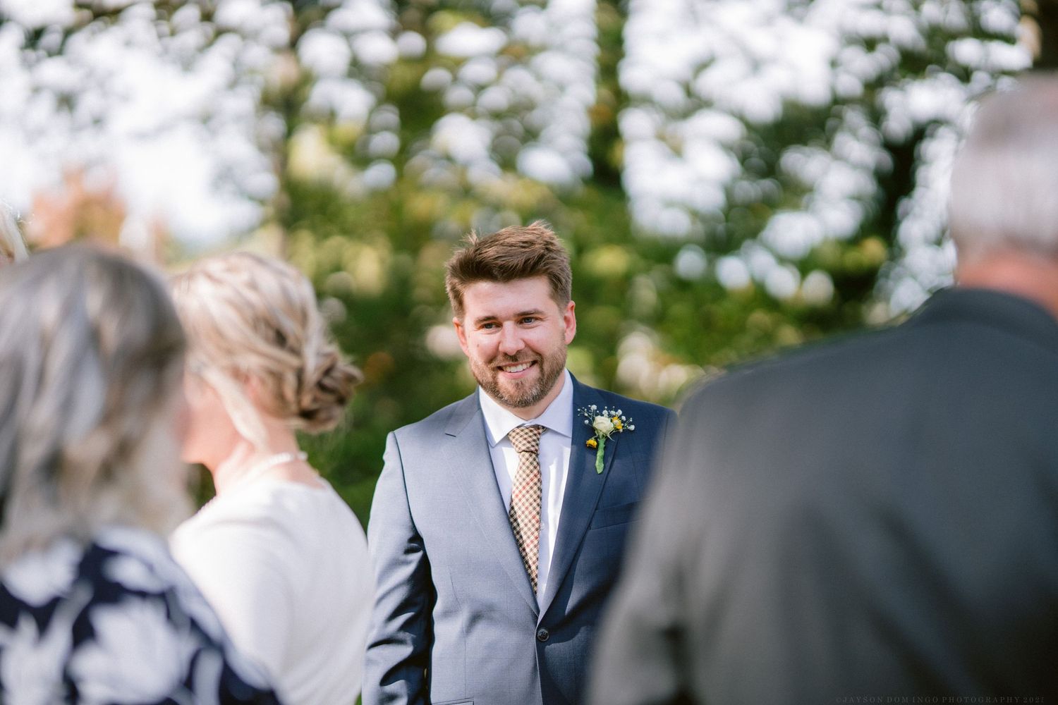 Wedding party members stand in formal attire during an outdoor ceremony.