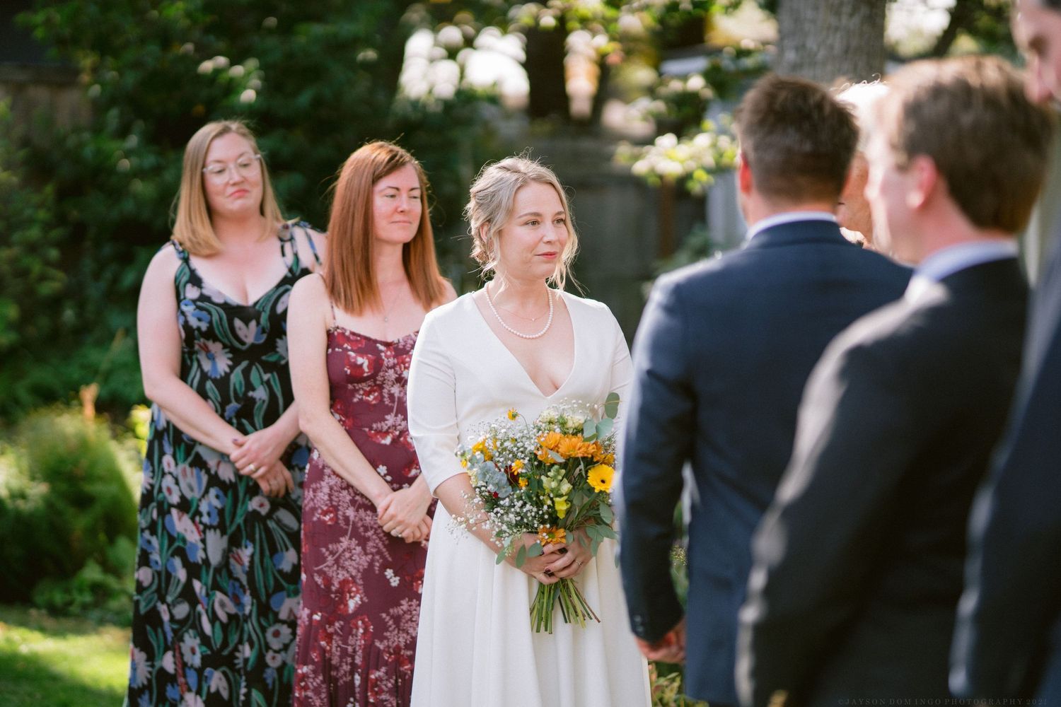 Wedding party gathered outdoors with vibrant sunflowers and summer dresses in natural lighting.
