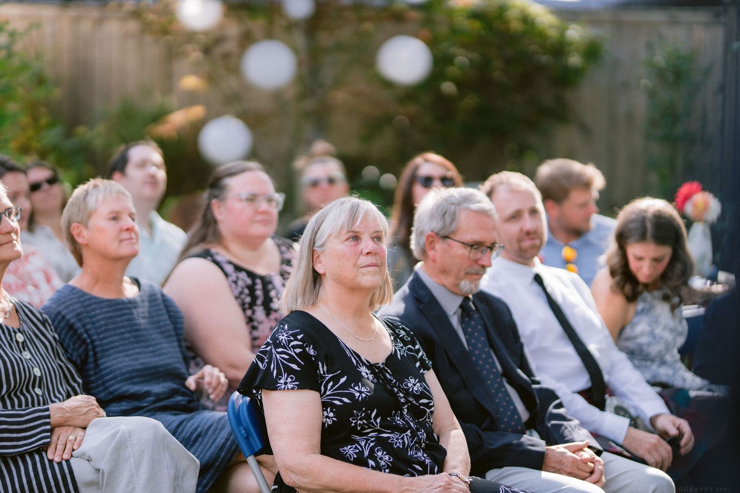Wedding guests seated outdoors watch the ceremony proceedings.