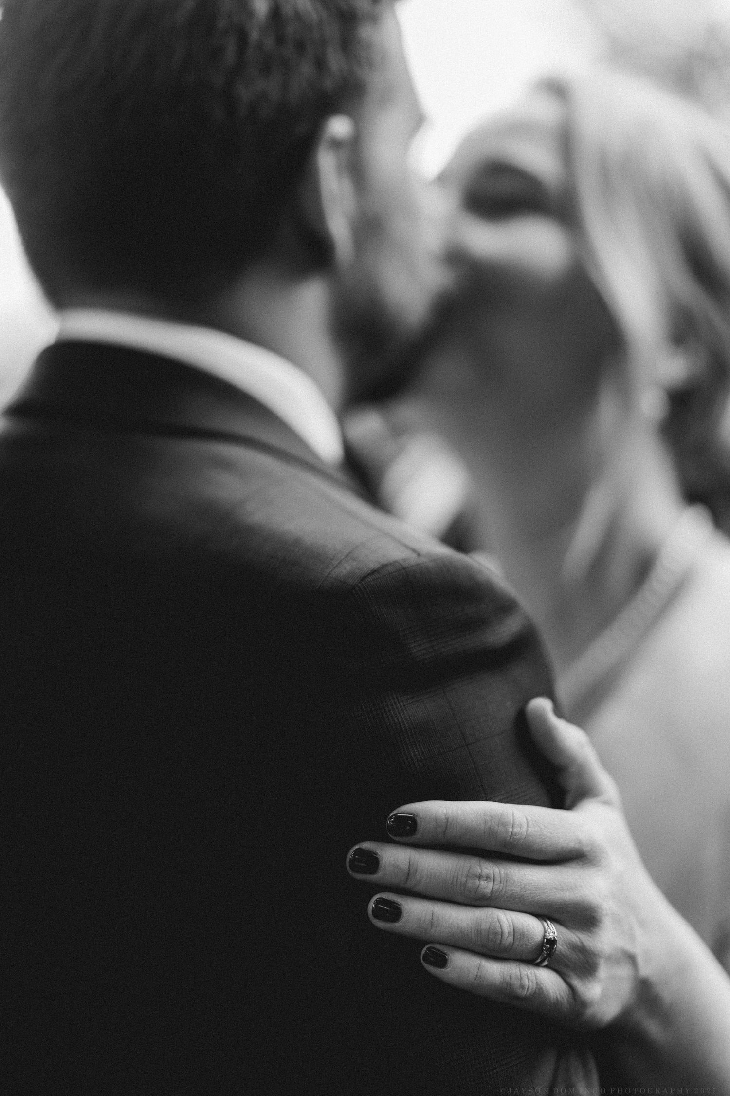 A black and white close-up photograph shows a hand resting gently on someone's shoulder in an intimate moment.