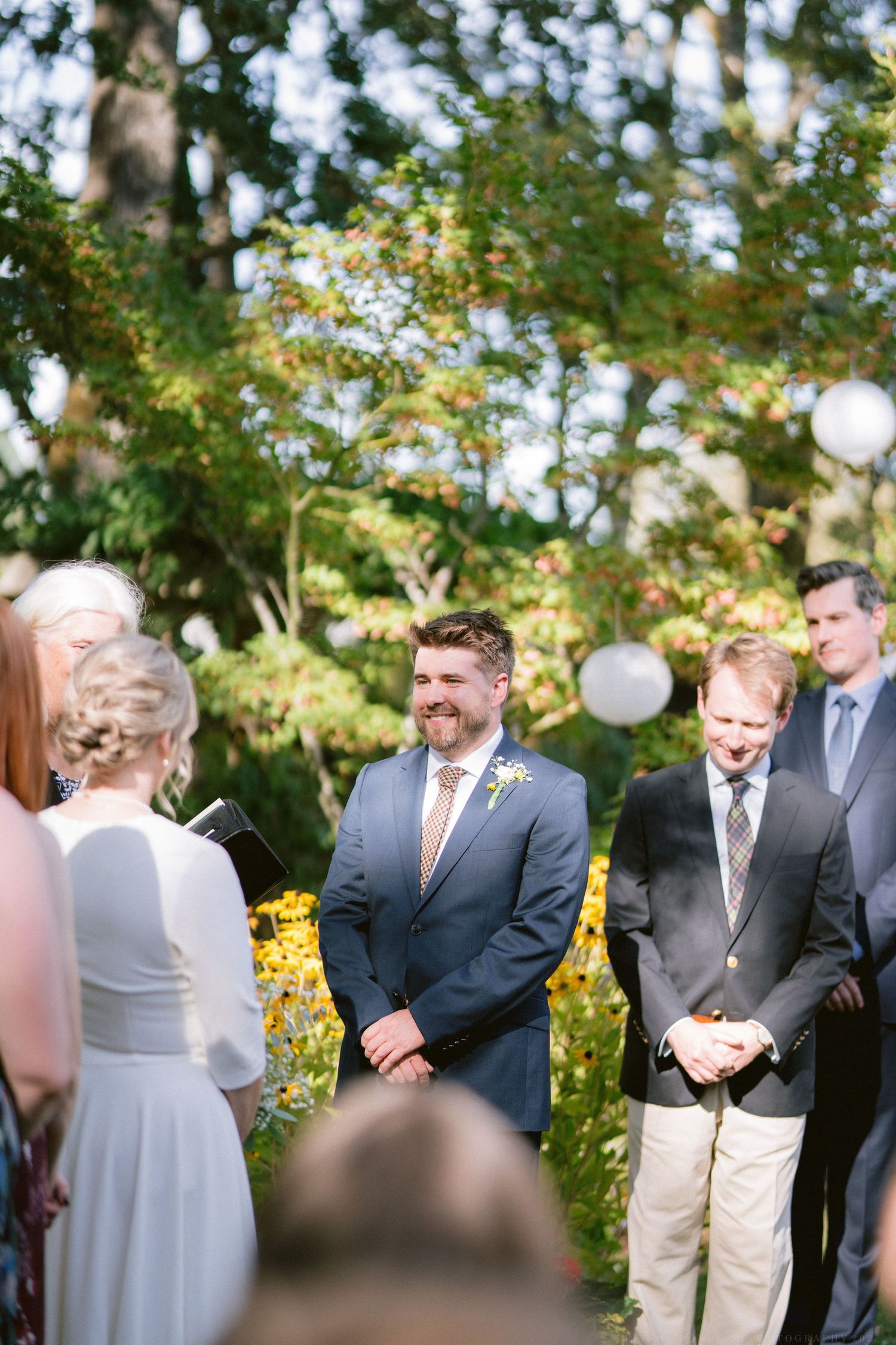 An outdoor wedding ceremony in a garden setting with yellow flowers and white balloons decorating the space.