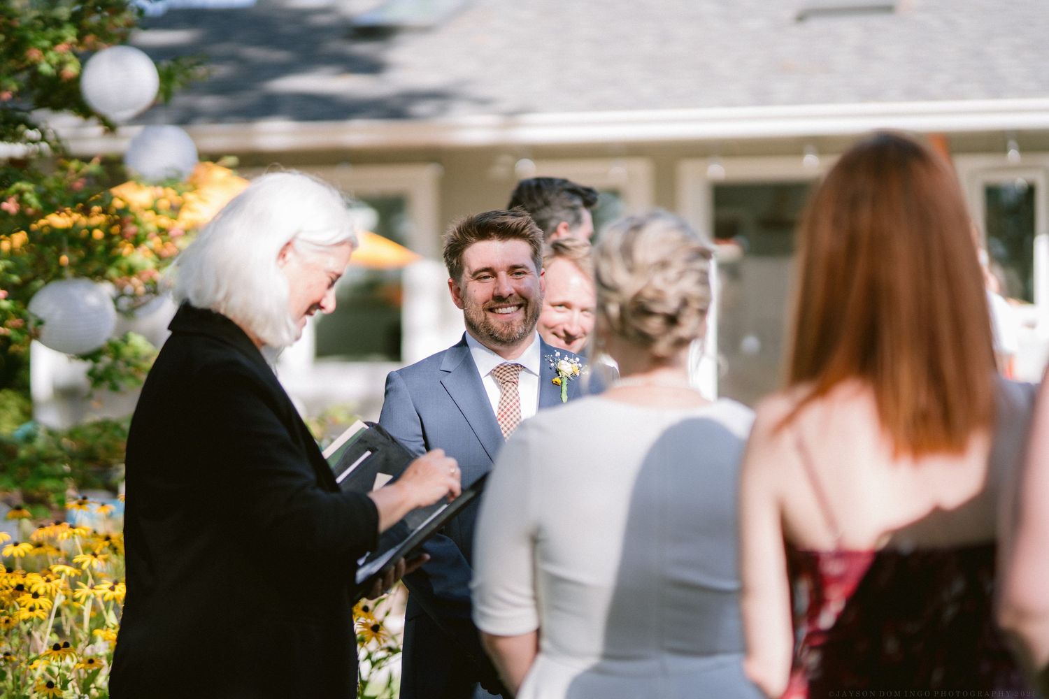 A candid moment during an outdoor wedding ceremony with guests gathered on a sunny day.