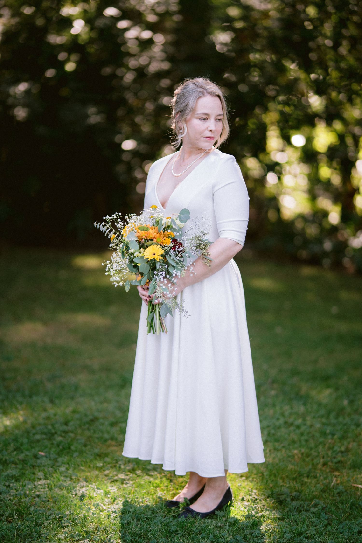 White dress and wildflower bouquet with yellow and green florals photographed in dappled sunlight.