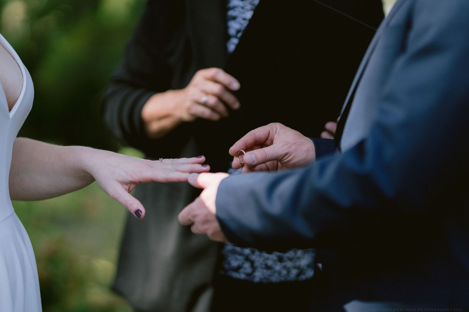 Close-up of hands exchanging rings during an outdoor wedding ceremony.