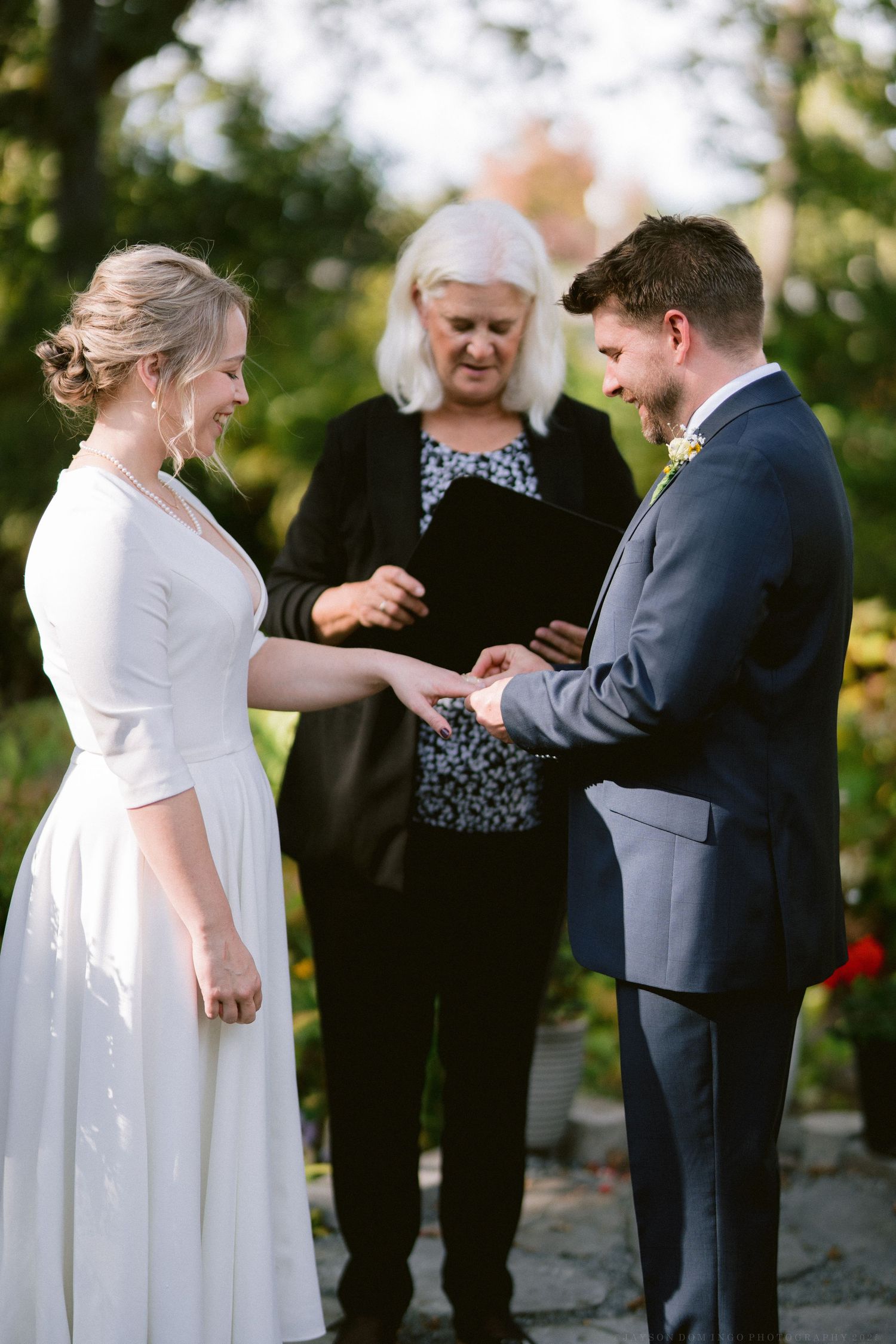 An intimate outdoor wedding ceremony showing the exchange of rings between the couple.