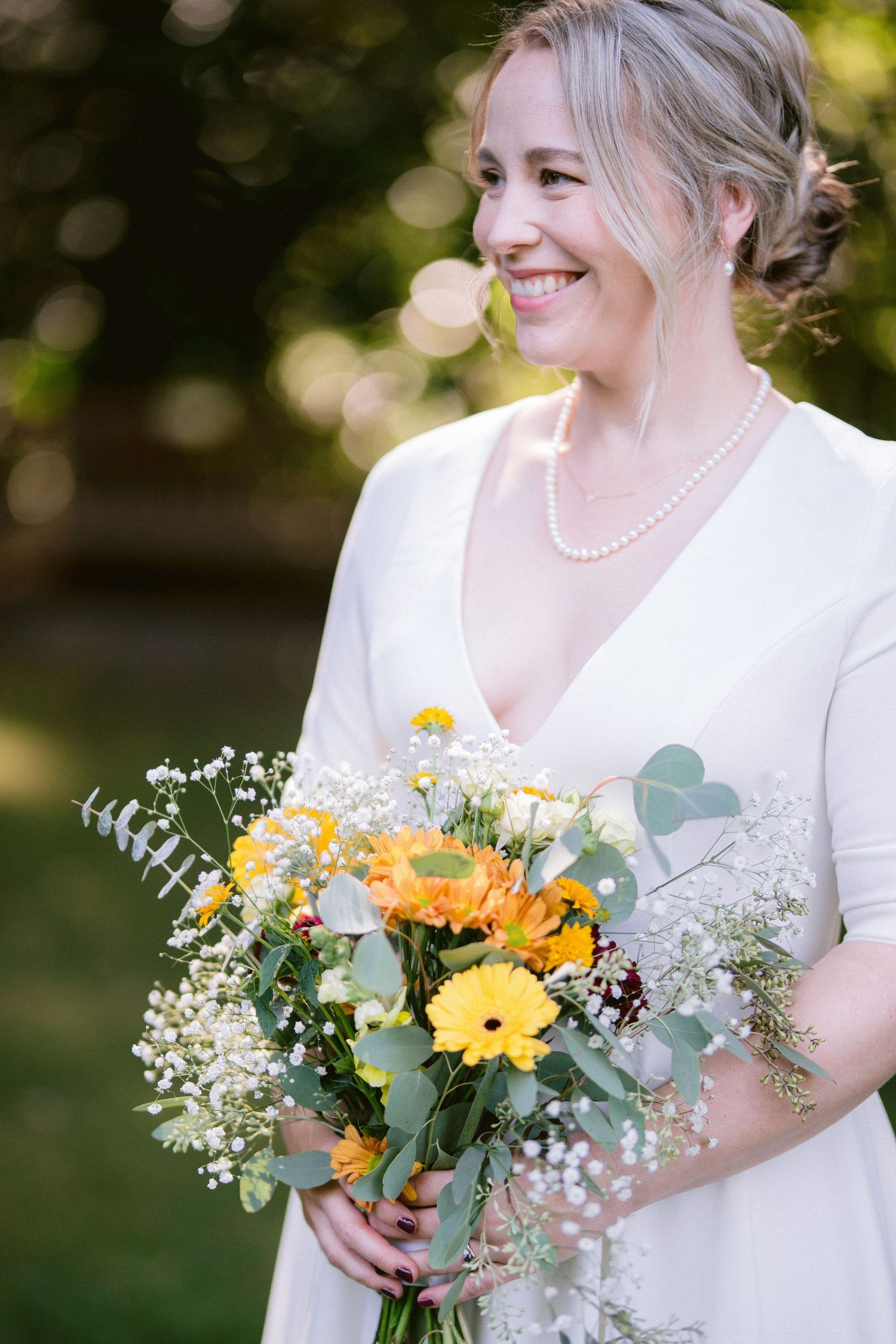 Bride in white dress holds vibrant yellow and white wildflower bouquet with eucalyptus.