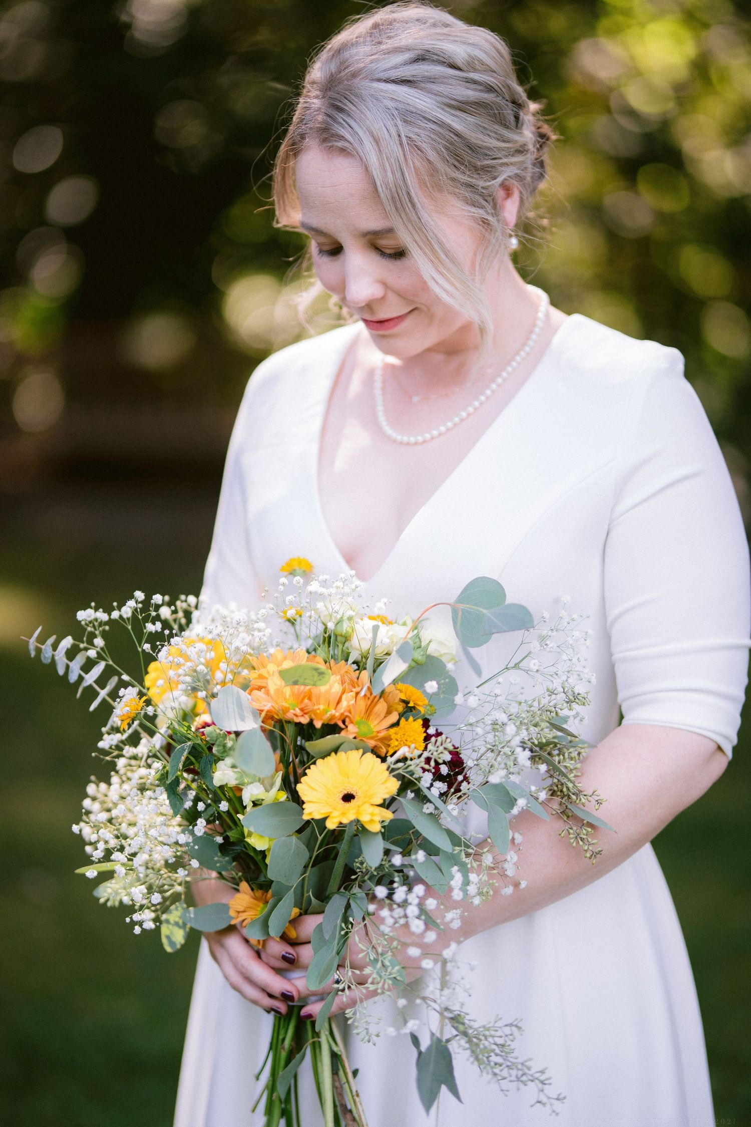 A bridal bouquet features bright yellow gerbera daisies, eucalyptus leaves, and white flowers against a white dress.