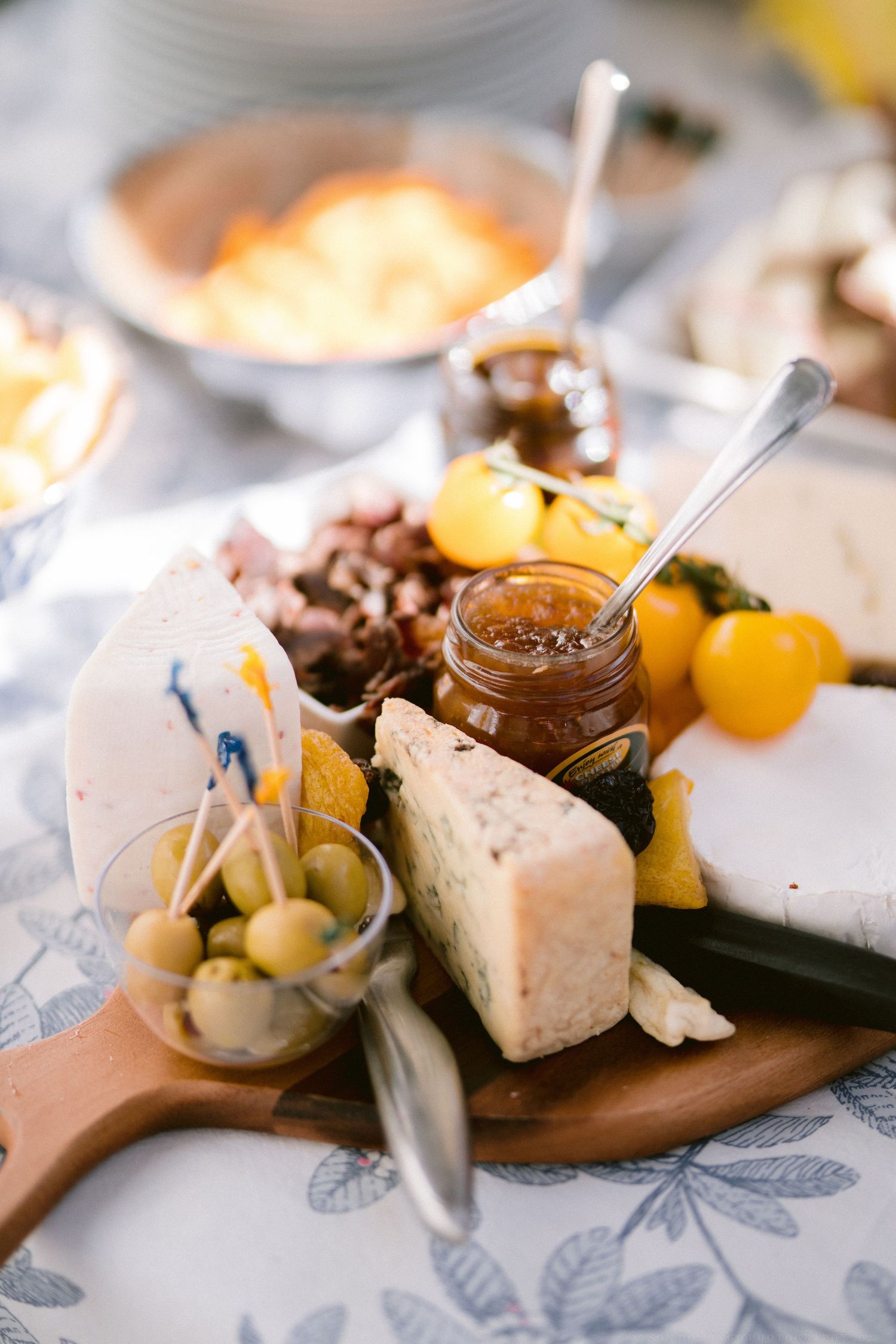 Elegant cheese and charcuterie board with jams and fruits served on a floral patterned tablecloth.