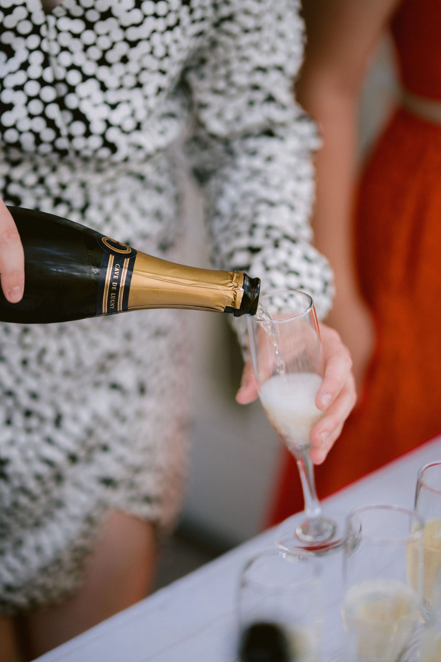 Champagne being poured into glasses against a white textured background.
