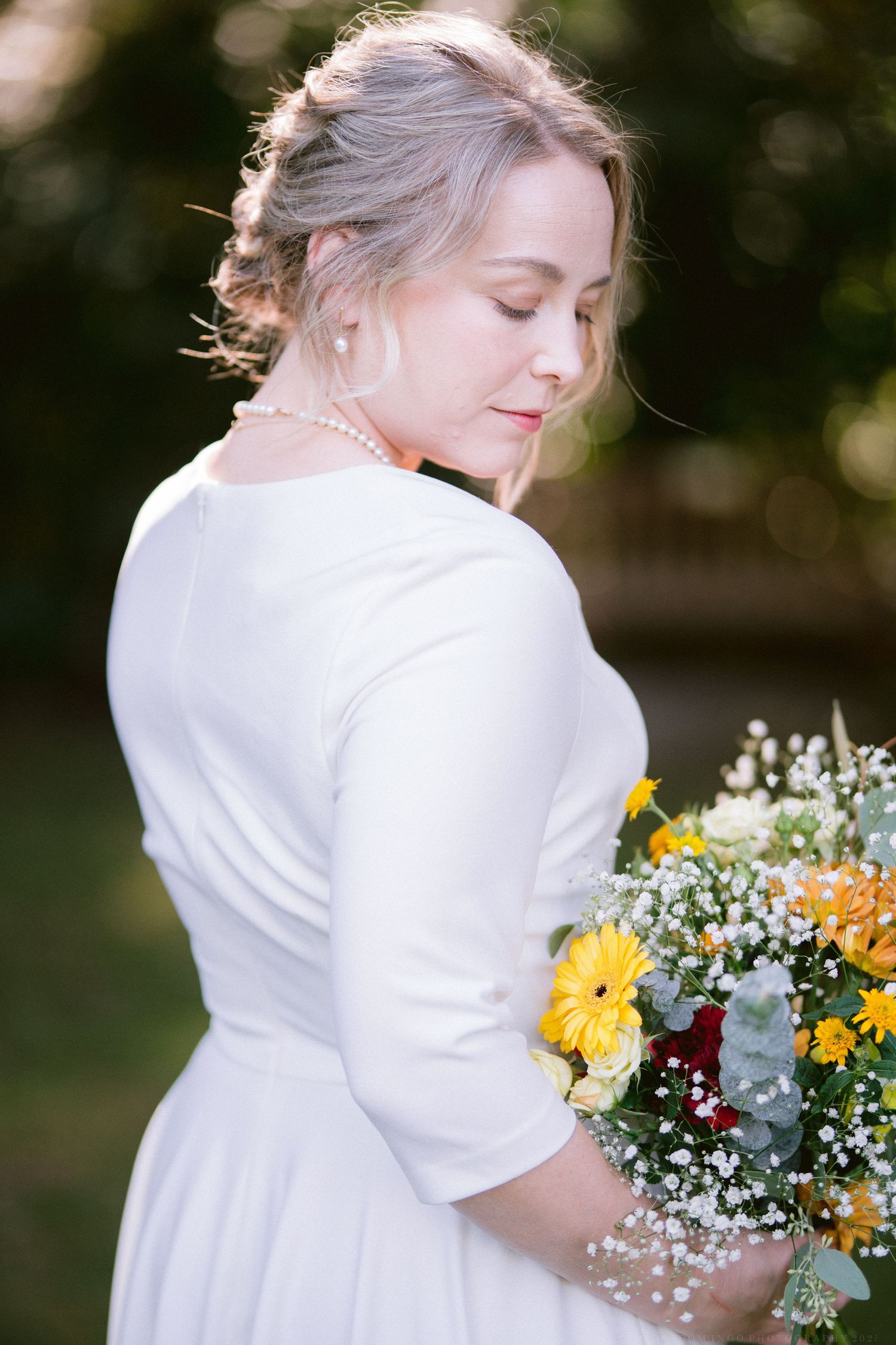 Close-up of bride holding rustic bouquet with yellow daisies, baby's breath, and eucalyptus leaves.